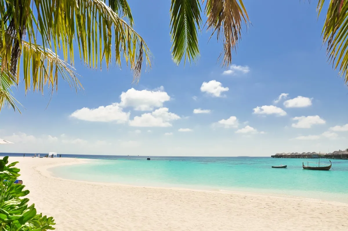 A boat on a white sand beach with turquoise water in the Maldives